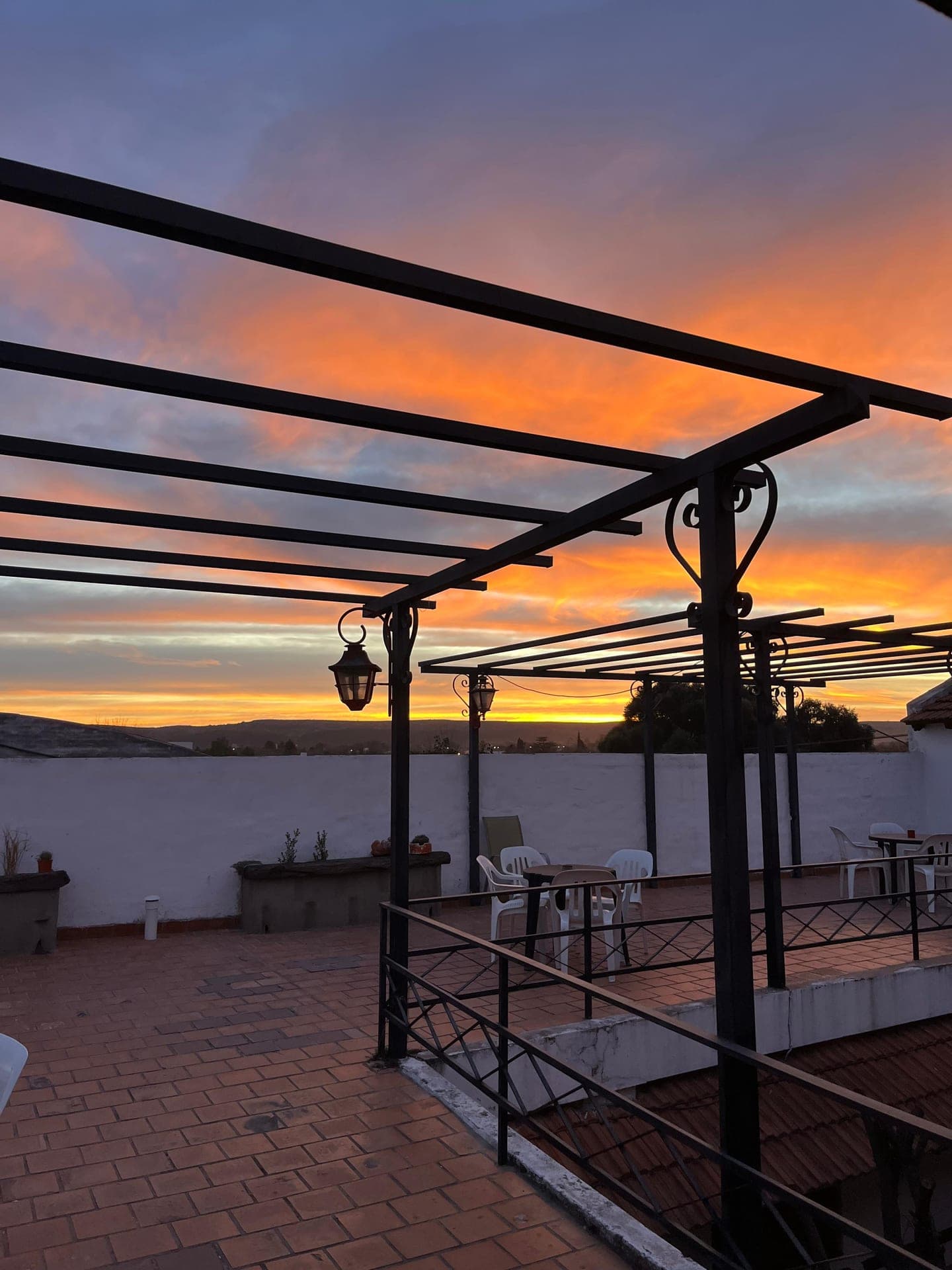 La terraza con pergolas de hierro al atardecer, con el cielo naranja