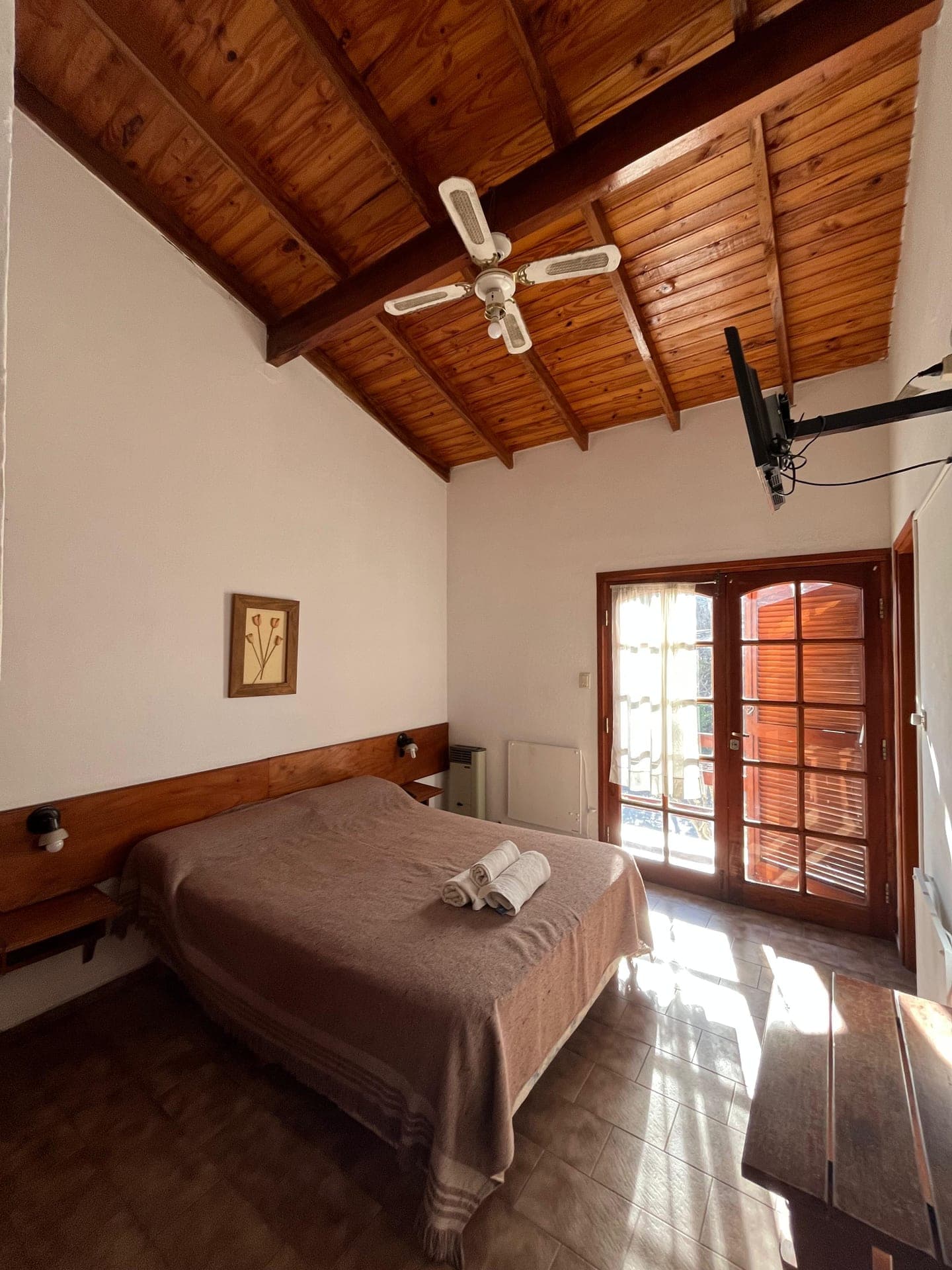 Habitacion con cama matrimonial, techo de madera a dos aguas y ventilador de techo