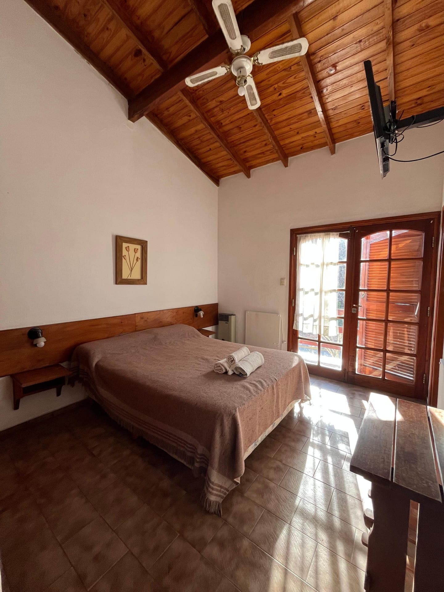 Habitacion luminosa con cama matrimonial y puerta ventana con postigos de madera