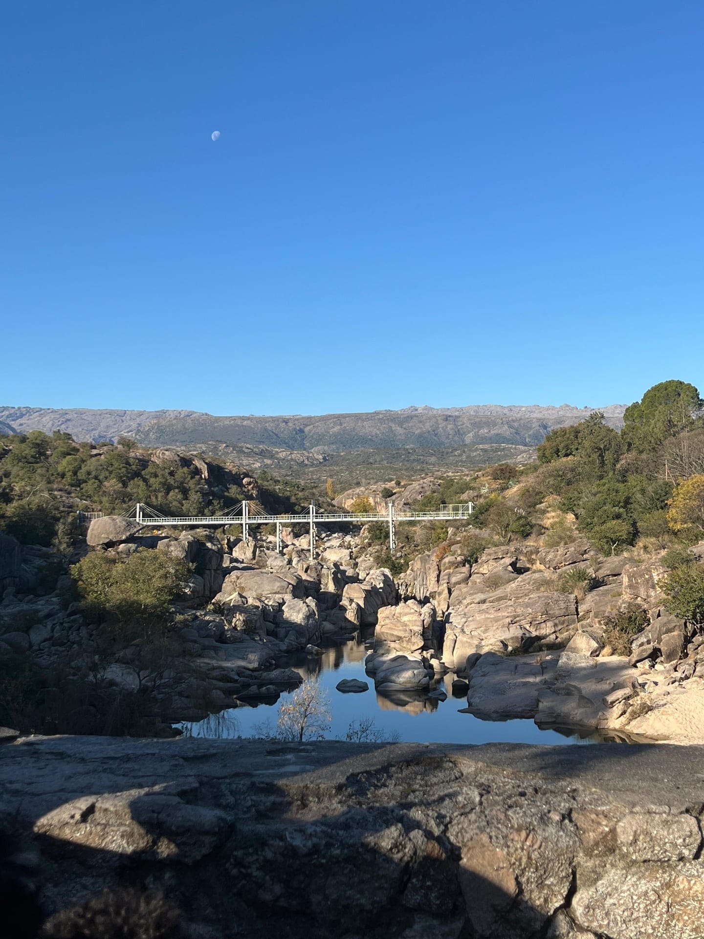 La pasarela colgante sobre el rio con la luna en el cielo
